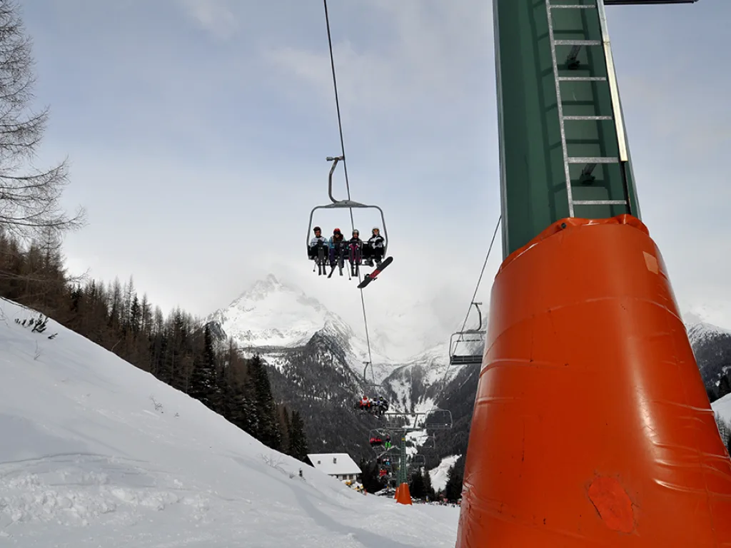Sessellift vor verschneiten Bergen, im Vordergrund eine orange Stütze.